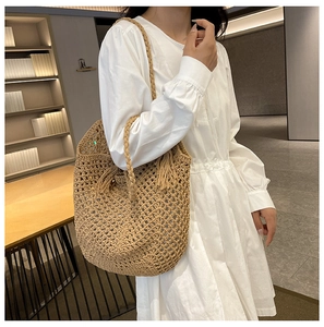 Detail of hollow woven straw tote bag with tassel decoration and mesh texture for summer