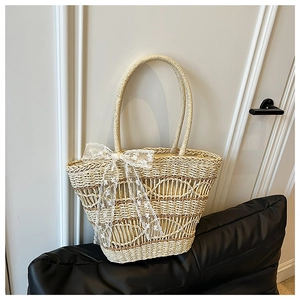 Detail of woven straw tote bag with elegant white lace bow and wave-hollow patterns