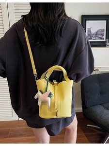 Modern bright yellow pebbled leather bucket bag with horse charm and crossbody strap
