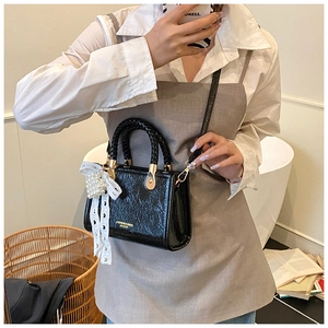 Model showing a black glossy crossbody bag with pearl heart and lace bow charm