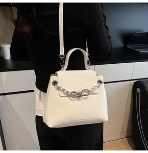 Detail showing creamy white leather texture with silver chain and brand logo