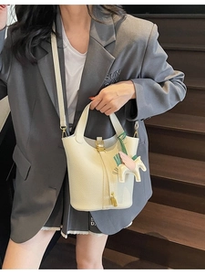 Beige bucket bag with lychee texture featuring a gold lock and leather horse pendant