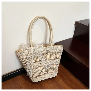 Close-up of woven straw tote bag featuring a white lace bow detail and textured finish