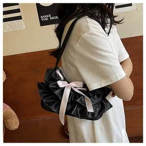 Detail of black satin pleated shoulder bag featuring a decorative pink silk bow and zipper
