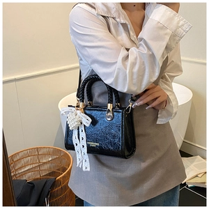 Close-up of black textured leather handbag featuring white lace bow and pearl heart charm