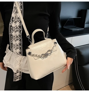 Close-up of white crossbody bag featuring silver chain detail and sleek metal knot clasp