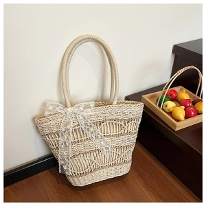 Detail of hand-woven straw tote bag with a white lace bow against a wooden floor