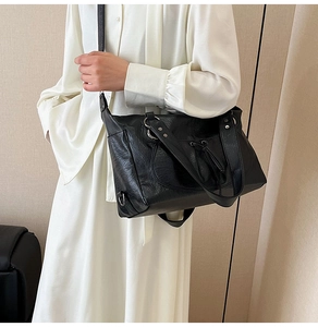 Detail of black tote bag with vintage pleated texture and silver ring on a white dress