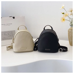 Close-up of stylish nylon mini backpacks in beige and black with metallic logo plaque