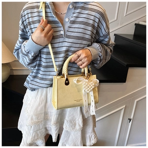 Detail of light yellow crossbody bag with woven handle and heart pearl charm ornament
