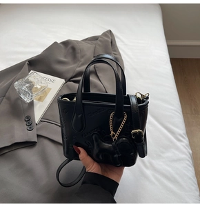 Détail du sac seau noir texturé avec charm chiot et bandoulière réglable tenu à la main