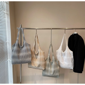 Detail of four woven canvas tote bags in different plaid patterns hanging on a metal rack