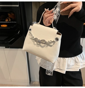 Close-up of cream white handbag featuring a silver metal bow and woven chain detail
