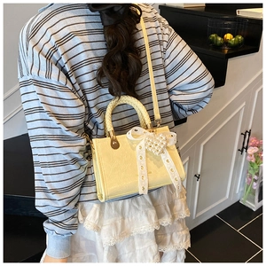 Close-up of a cream crossbody bag with woven handle and lace bow in a lifestyle setting