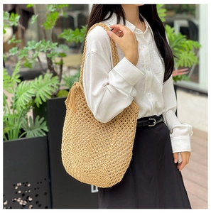 Détail d'un sac cabas beige en paille tressée avec bandoulière et pendentif à pompon