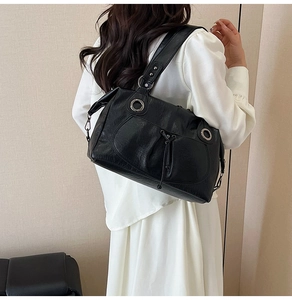 Detail of black glossy tote bag with large silver grommets on a white shirt dress