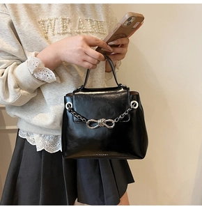 Detail of glossy black handbag featuring silver chain strap and a bow-shaped metal clasp