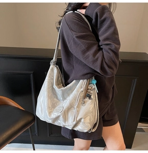 Silver metallic tote bag with ripple texture and bear charm worn by a model