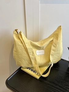 Yellow nylon crescent shoulder bag with wide strap and brand label on desk