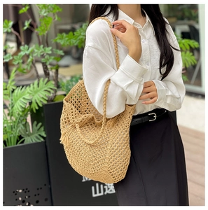Détail d'un sac à bandoulière en paille tissée ajourée avec pompon et maille filet