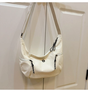 Détail du sac demi-lune crème montrant la texture en nylon et la large bandoulière réglable