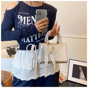 Detail of silver handbag featuring a pearl heart charm and lace bow decoration