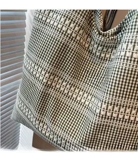 Close-up of green checkered canvas tote bag showing soft fabric and white wavy embroidery