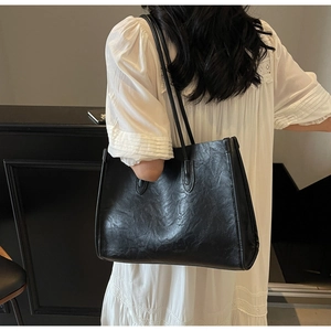 Rear view of a black matte PU leather tote bag worn by a model in a minimalist setting