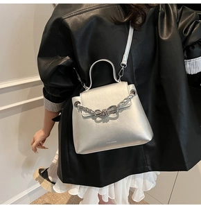 Silver metallic crossbody bag with bow chain detail shown on shoulder of a model