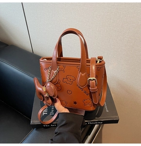 Détail d'un sac seau marron montrant des motifs de chiots embossés et un charme assorti