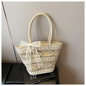 Detail of hand-woven straw tote bag with delicate hollow patterns and a white lace bow