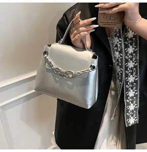 Detail of silver chain handbag with metallic bow clasp on a model in a black leather jacket