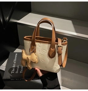 Détail d'un sac seau crème avec motif chien gaufré et pendentif sur un escalier gris