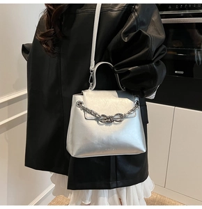 Detailed shot of silver crossbody bag featuring a metallic bow chain and leather top handle