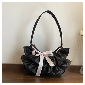 Detail of black pleated underarm bag with a pink silk ribbon bow on a wooden surface