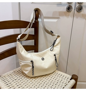 Détail du sac croissant crème avec poches zippées latérales et logo sur tissu texturé