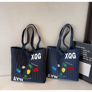 Detail of blue striped denim tote bags featuring XQG and AYW lettering on white surface