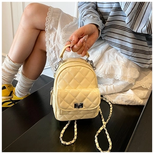 Detail of light yellow quilted patent leather backpack with chain strap and metal lock
