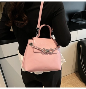 Close-up of pink leather crossbody bag with silver chain bow and brand logo