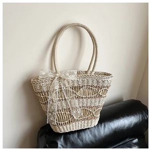 Detail shot of a beige straw tote bag with intricate white lace bow decoration