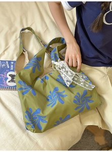 Detail of olive green nylon crescent bag with blue floral print and white lace bow