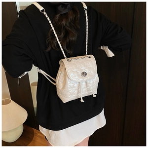 Detail of white star-quilted leather backpack with silver turn-lock and chain strap on model