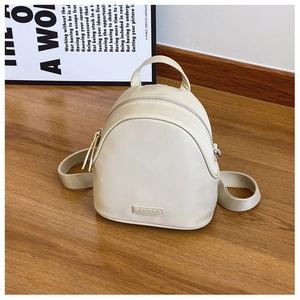 Detail shot of a minimalist cream-white mini backpack with silver metal zipper on wood floor