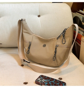 Détail du sac demi-lune beige avec tirettes décoratives et logo métallique discret