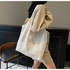 Detail of white canvas tote bag featuring textured fabric and delicate lace embroidery