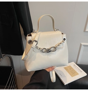 Close-up of cream square bag featuring a metal woven chain and bow-shaped twist lock