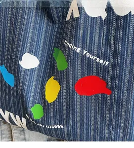 Detail of blue striped denim tote showing colorful graffiti prints and artistic text