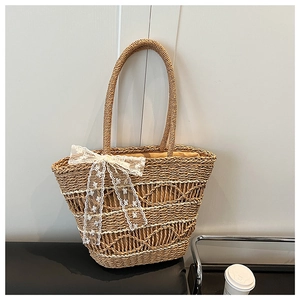 Close-up of woven straw tote bag with large white lace bow in minimalist urban setting