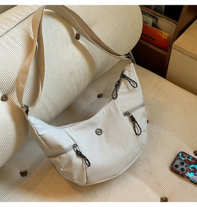 Détail d'un sac besace en nylon crème avec plusieurs poches zippées et un logo métallique
