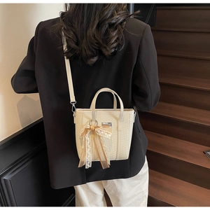 Dettaglio mini borsa a secchiello intrecciata bianco sporco con ciondolo a fiocco in pizzo e PU
